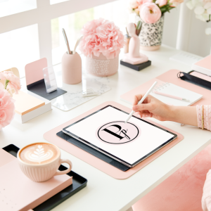 A stylish pink workspace with an iPad, coffee, and soft floral decor, setting the tone for a post about personalized gifts and custom home accents.