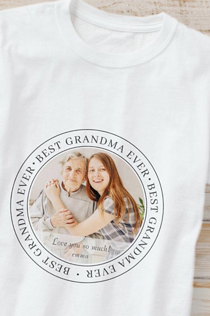 White T-Shirt With A Circular “Best Grandma Ever” Design Featuring A Custom Photo Of Grandma And Granddaughter, Plus A Personalized Message.