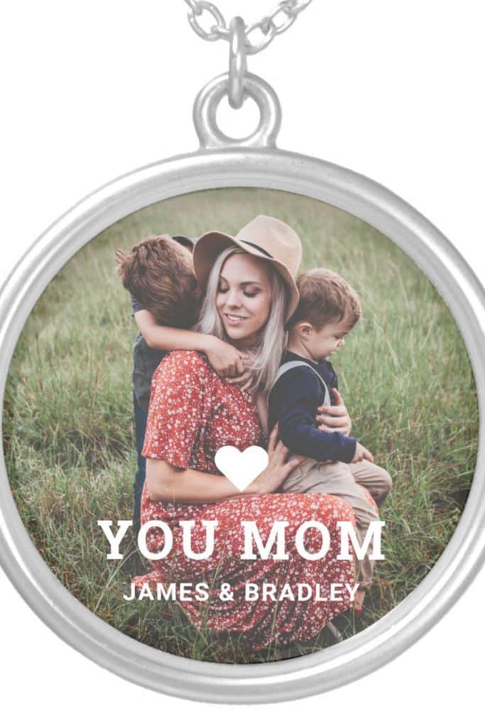 Round Silver Pendant Necklace With A Photo Of A Mom And Two Sons In A Field, “Love You Mom” Text And “James &Amp; Bradley” Printed Below.