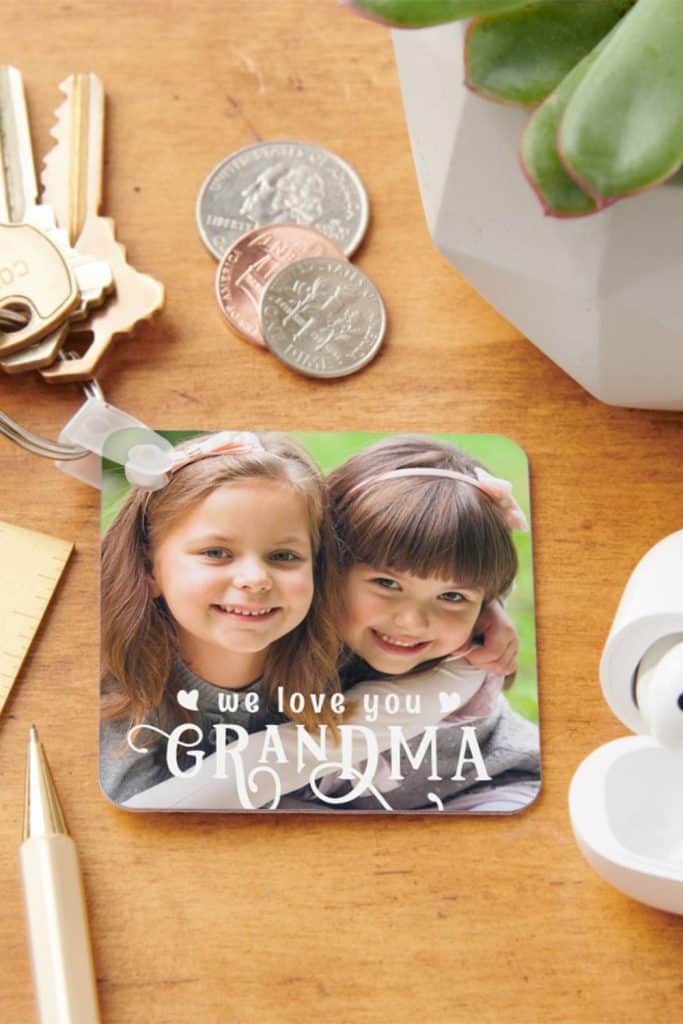 Square Keychain With A Custom Photo Of Two Smiling Girls And The Message “We Love You Grandma” In White Text—Personalized Mother’s Day Gift For Grandma.