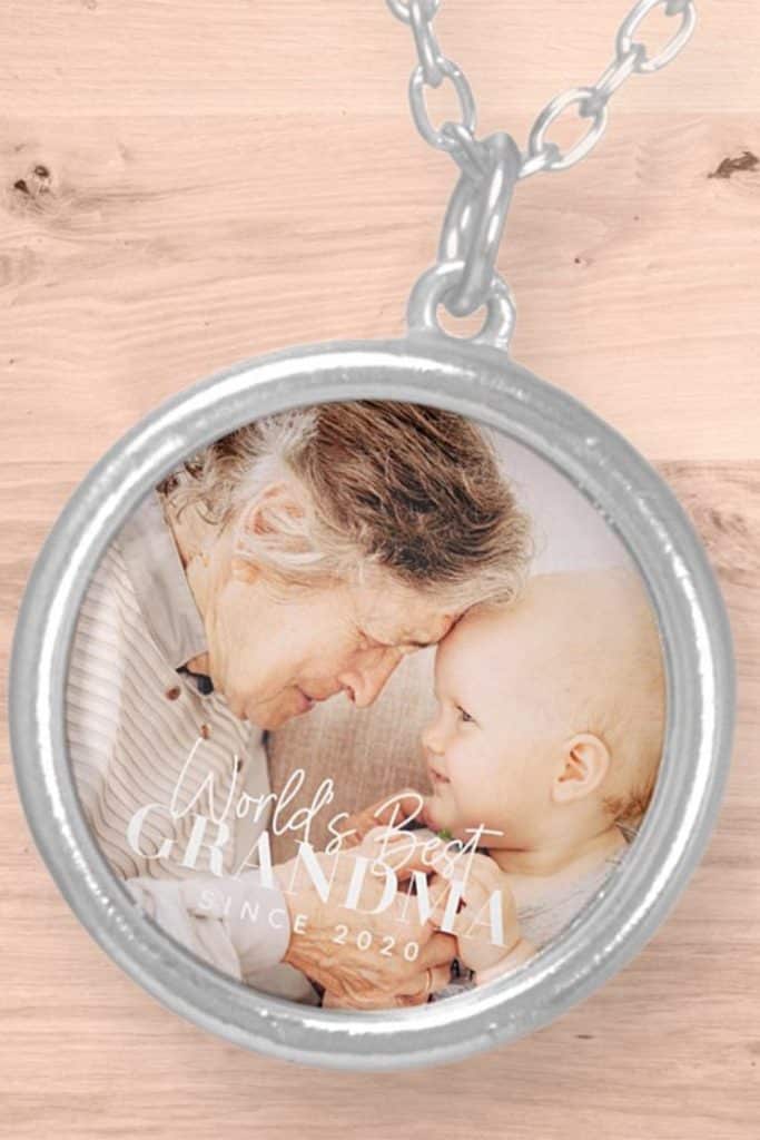 Round Silver Necklace With Photo Of Grandma And Baby Touching Foreheads, “World’s Best Grandma Since 2020” Text In Modern White Script.