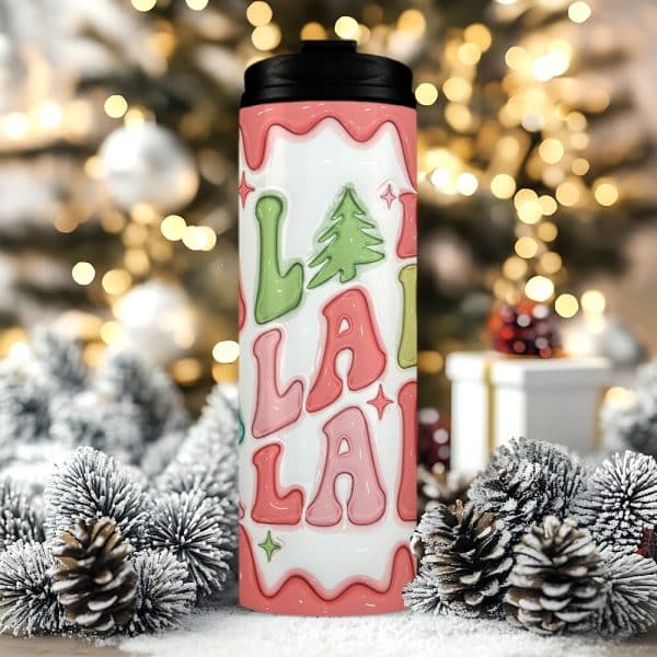 A Christmas-Themed Travel Tumbler With A Pink And Green Lalala Design And A Small Evergreen Tree.