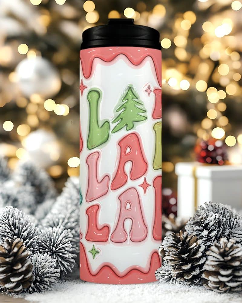 A Christmas-themed travel tumbler with a pink and green LaLaLa design and a small evergreen tree.