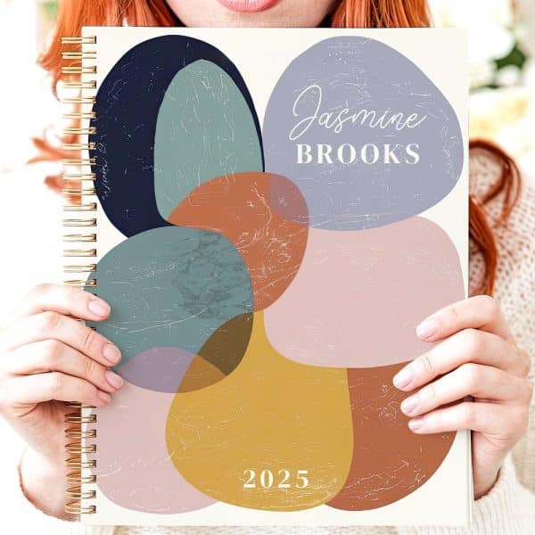 Person Holding A 2025 Planner With An Abstract Floral Design And Their Name, Jasmine Brooks.