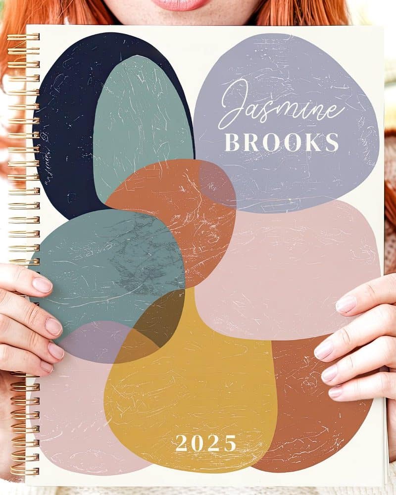 Person holding a 2025 planner with an abstract floral design and their name, Jasmine Brooks.