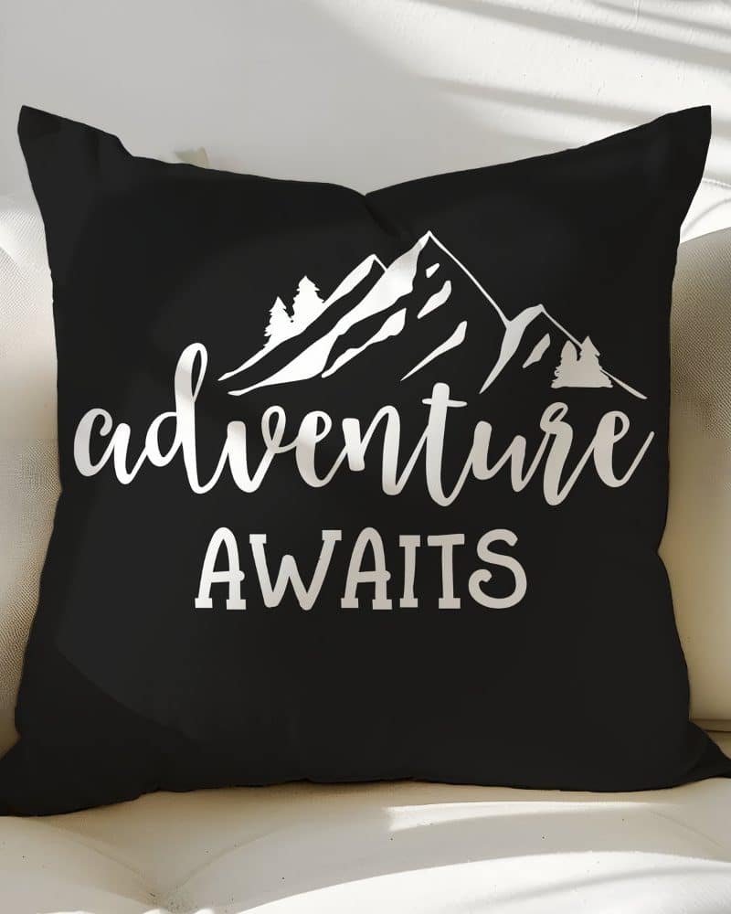 Black throw pillow with white mountains and trees design, and the text Adventure Awaits.
