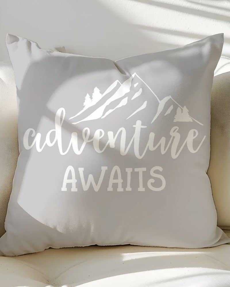 Light gray throw pillow with white mountain graphic and the text Adventure Awaits.