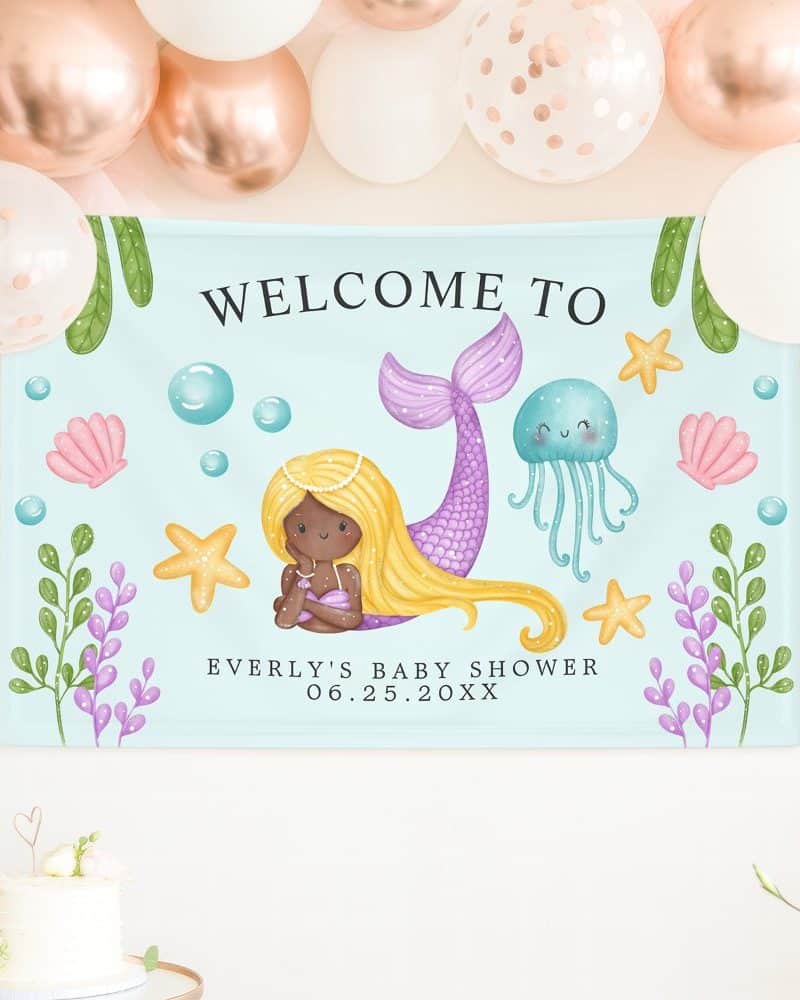 Baby shower banner featuring a mermaid with long blonde hair and a purple tail. The banner also includes seashells, starfish, and a jellyfish.