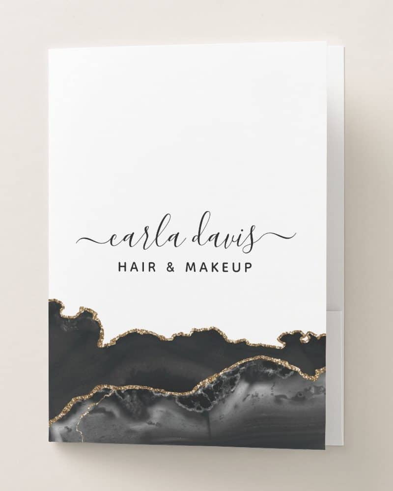 A white portfolio folder with Carla Davis Hair & Makeup written in elegant script, underlaid with a black and gold abstract design.