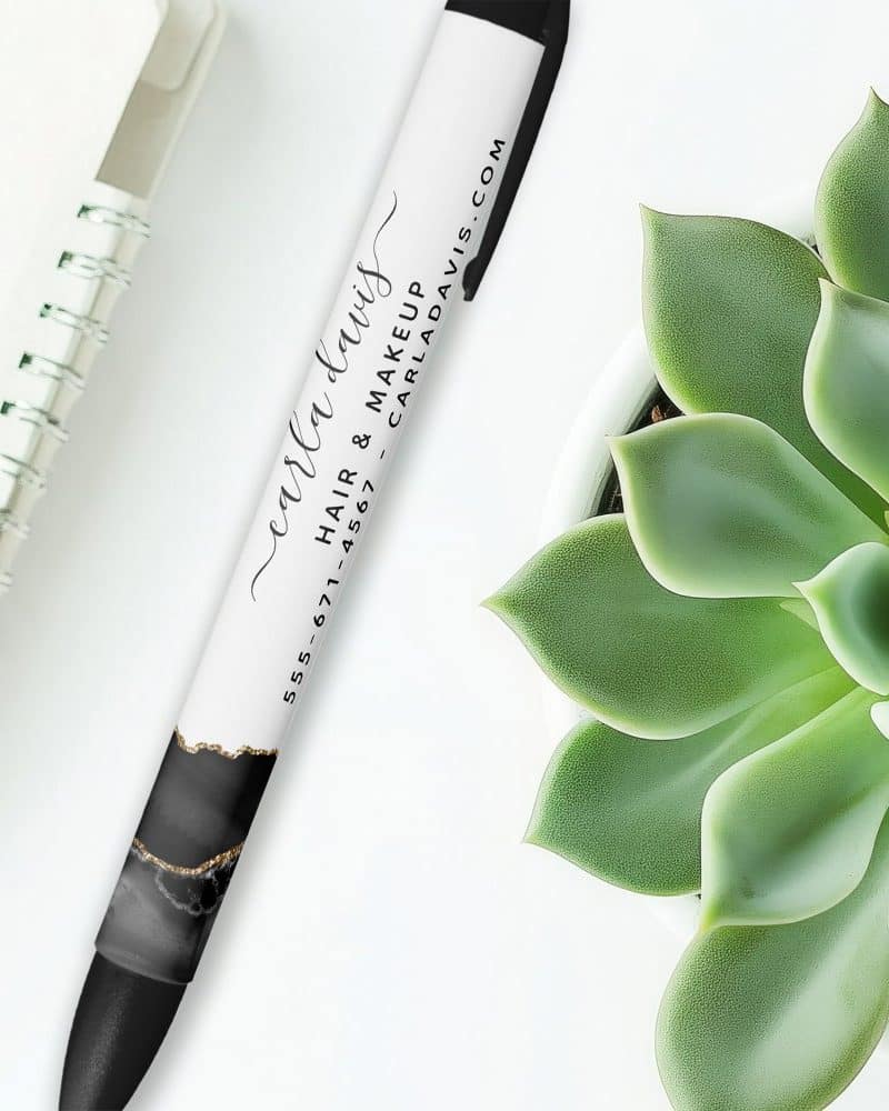 A pen with Carla Davis Hair & Makeup contact information and a black and gold marble design.