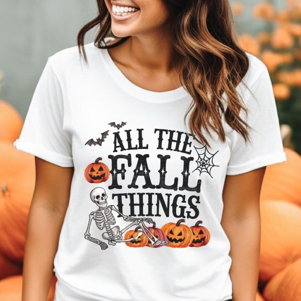 Woman Wearing A White T-Shirt With A Halloween Design Featuring A Skeleton, Pumpkins, Bats, And A Spiderweb. The Shirt Says All The Fall Things.