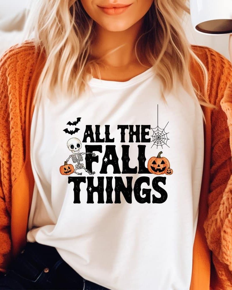 White shirt with a Halloween-themed design featuring a skeleton, pumpkins, and bats, and the text All the Fall Things.
