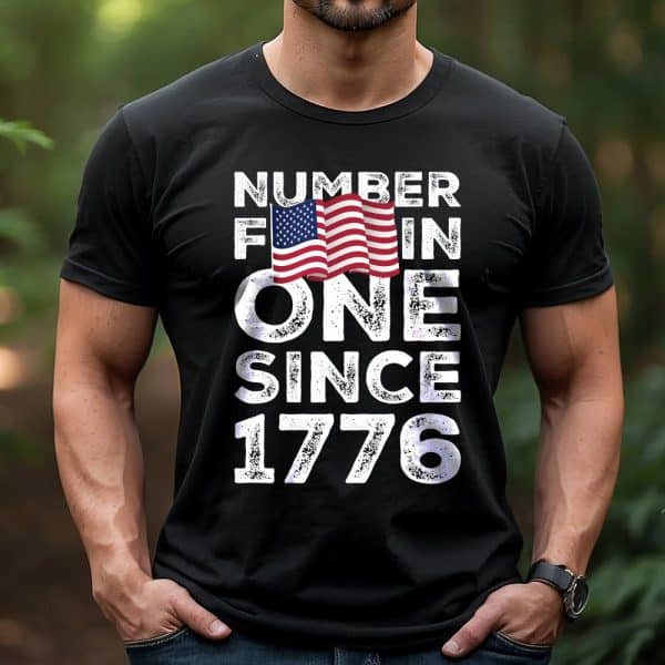 Man Wearing A Black T-Shirt With A Distressed American Flag Graphic And The Text Number 1 Since 1776.