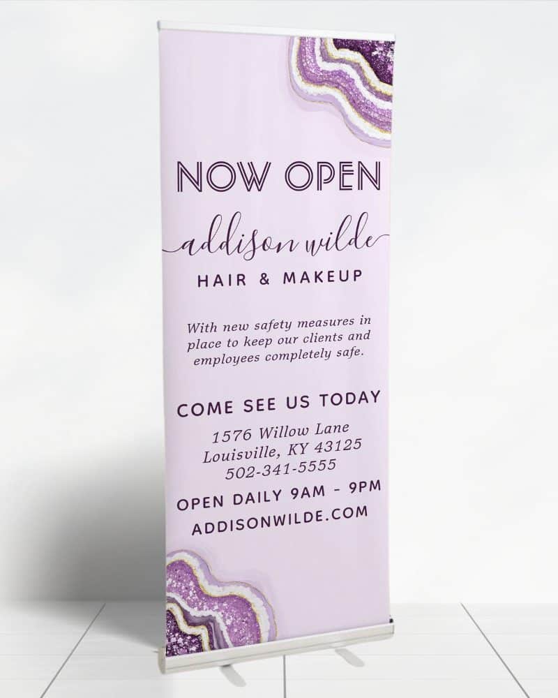 Retractible banner announcing the grand opening of Addison Wilde Hair & Makeup salon, including address and hours.