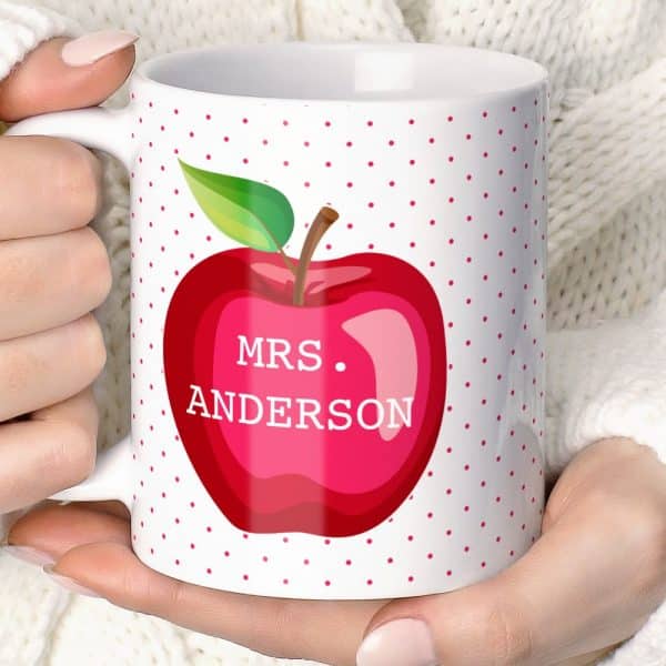 A White Coffee Mug With A Red Apple And Pink Polka Dots; The Name Mrs. Anderson Is On The Apple.