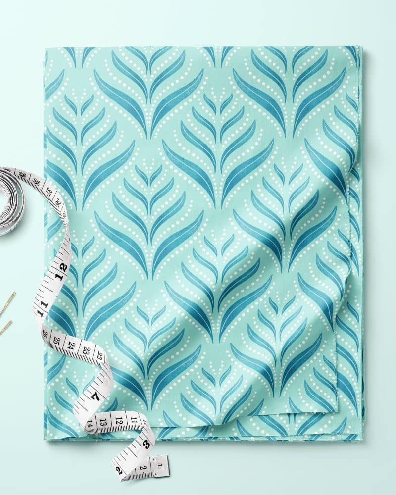 Teal fabric with a repeating leaf and dot pattern, accompanied by a tape measure and needles.