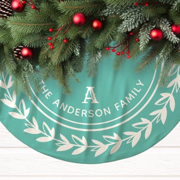 Teal Christmas Tree Skirt With The Anderson Family Name And A Large A In A Circular Design, Decorated With A Wreath Of Leaves. Pine Boughs With Red Ornaments Are Arranged At The Top.
