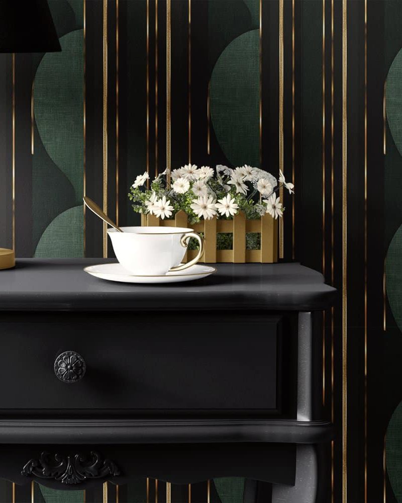 A black nightstand with a teacup and saucer, and a small plant in a wooden box sits in front of a dark green and gold patterned wall.