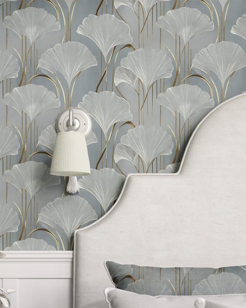 A curved headboard against a wall covered in light blue wallpaper featuring a repeating pattern of gold and white ginkgo leaves.