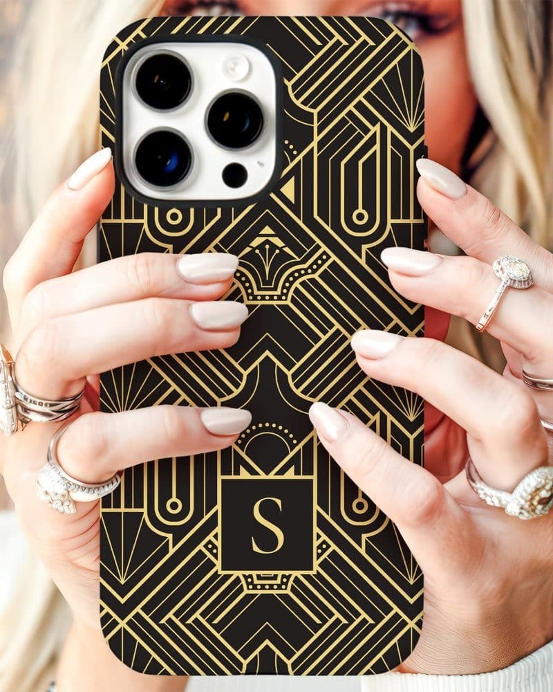 Hands holding a black iPhone case with a gold Art Deco design and the initial S.