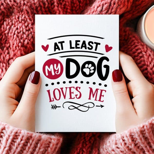 Two Hands Hold A Card That Says At Least My Dog Loves Me.