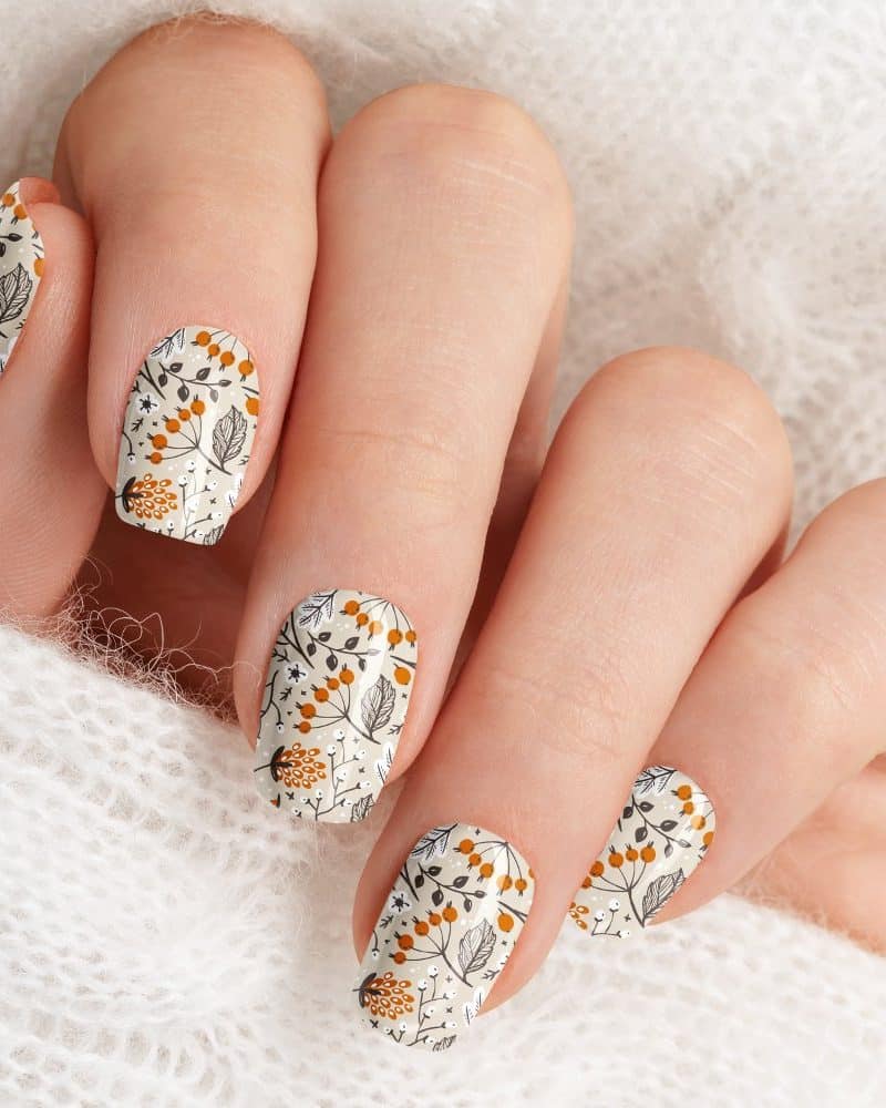 Close-up of a hand with fingernails adorned with an autumnal floral nail design.