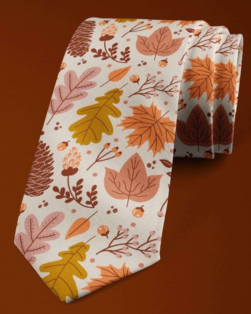 Off-white necktie featuring an autumnal leaf and pinecone pattern.