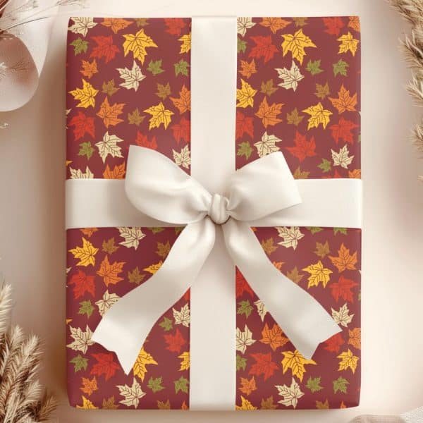 Autumn-Themed Gift Wrapped In Maroon Paper With A White Ribbon And Bow. The Paper Is Covered In A Pattern Of Colorful Maple Leaves.