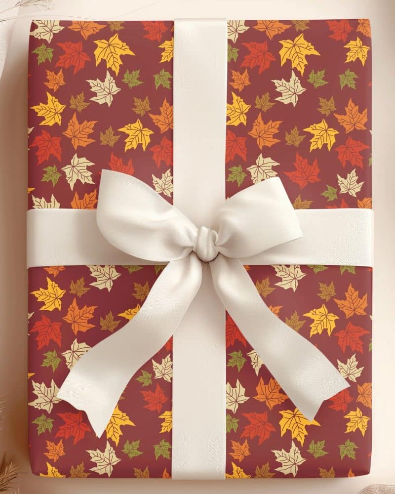 Autumn-themed gift wrapped in maroon paper with a white ribbon and bow. The paper is covered in a pattern of colorful maple leaves.