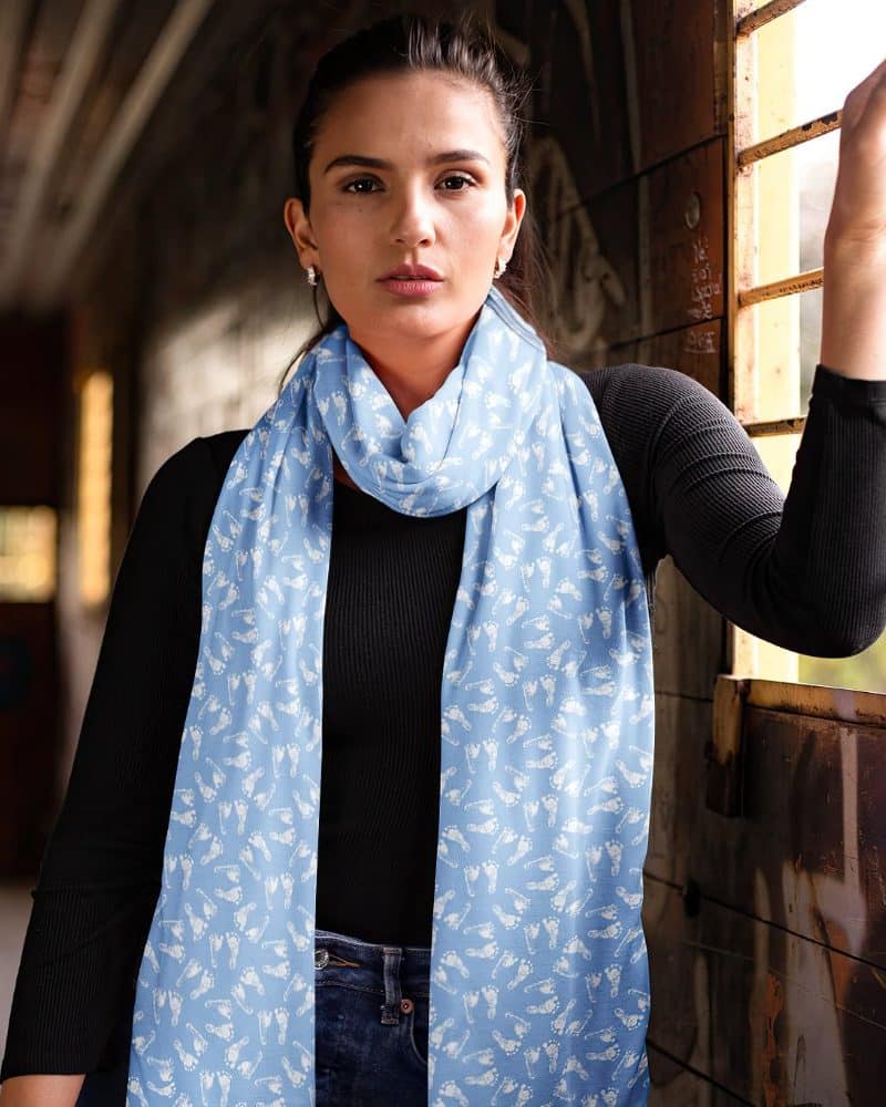 Woman wearing a light blue scarf with a white footprint pattern.