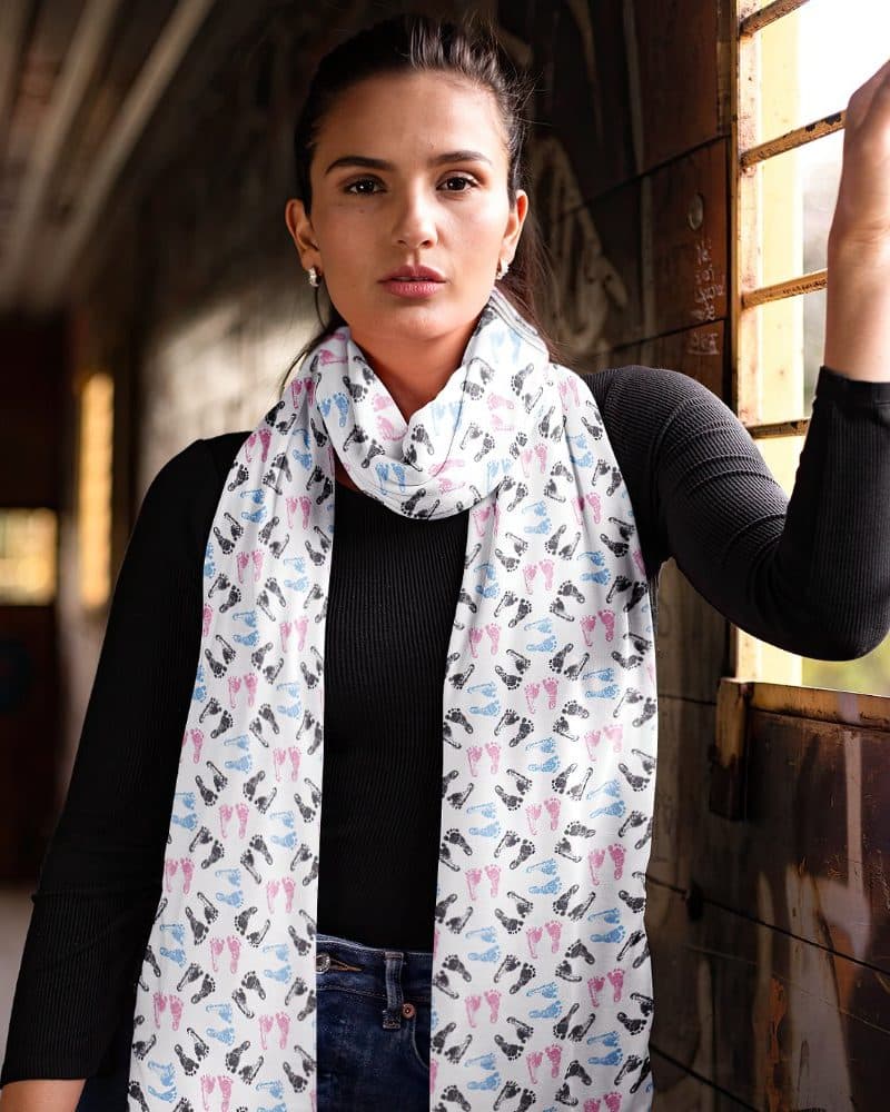 Woman wearing a white scarf with pink and blue baby footprints.