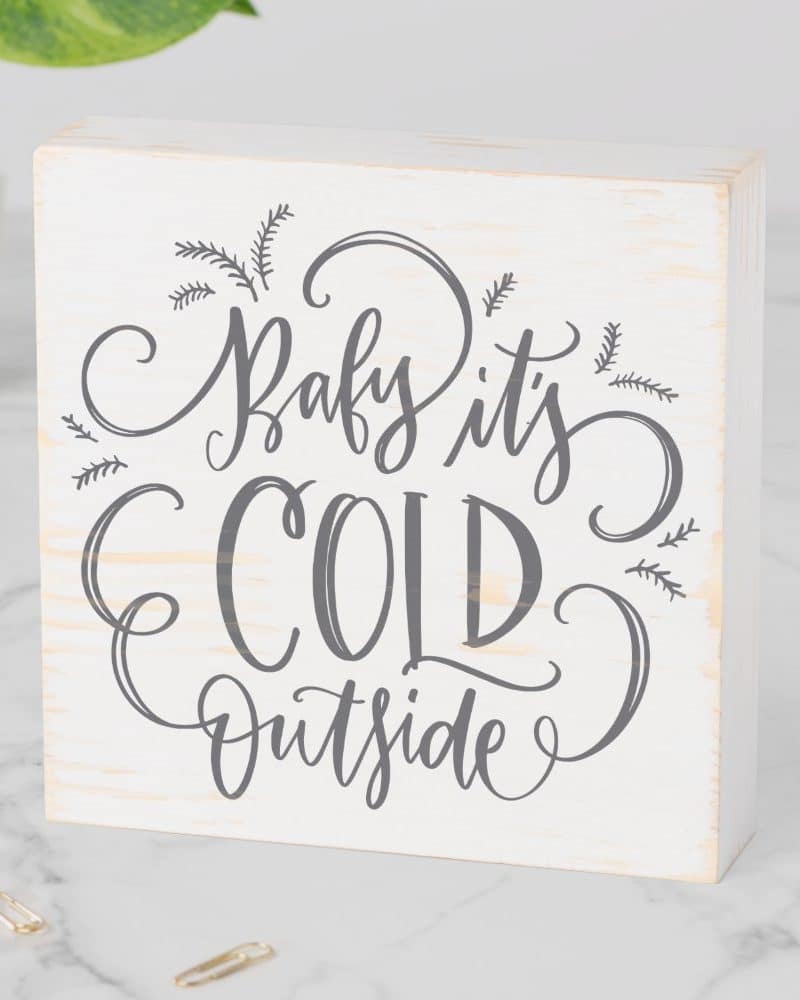 White wood block with gray lettering that says Baby It's Cold Outside.