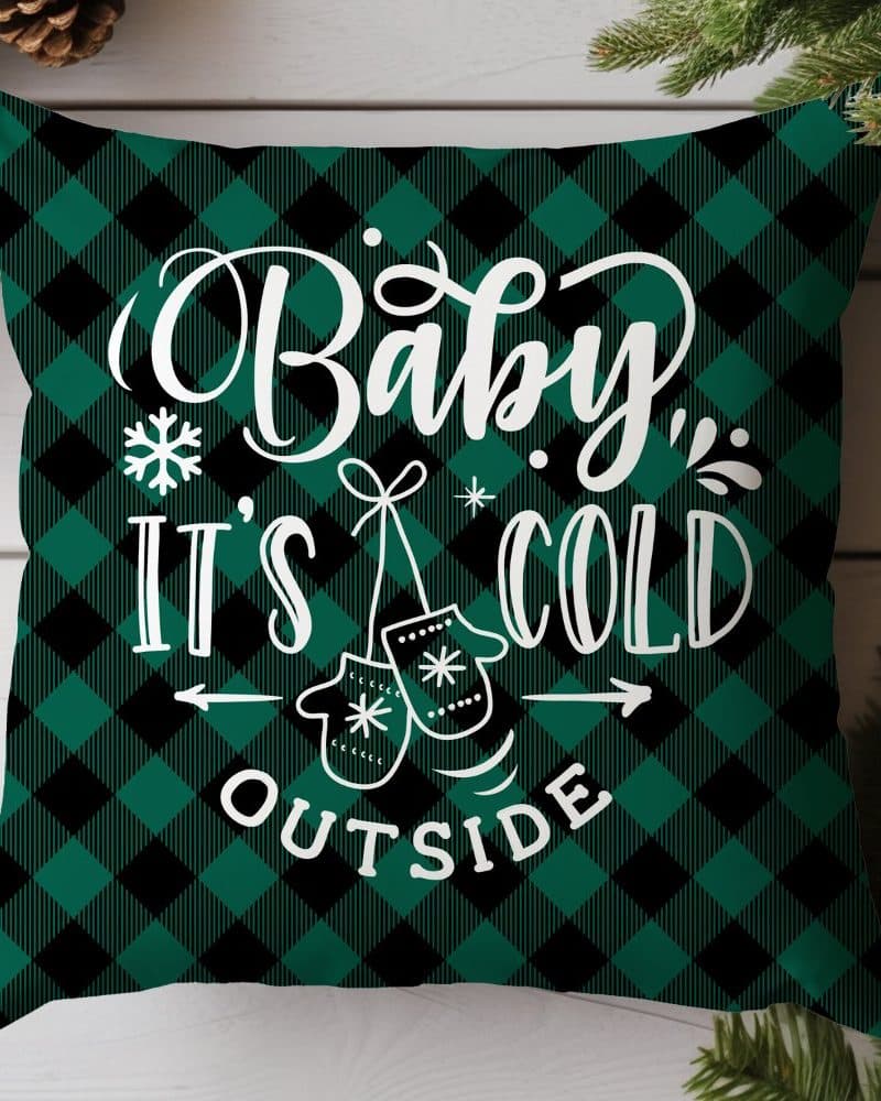 Green and black buffalo plaid throw pillow with the text Baby, It's Cold Outside and a pair of mittens.