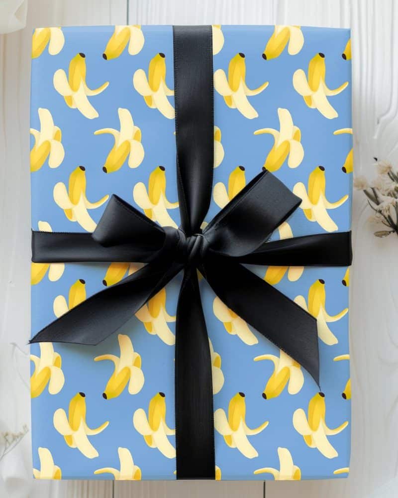 A gift wrapped in light blue paper with a pattern of peeled bananas and tied with a black ribbon.
