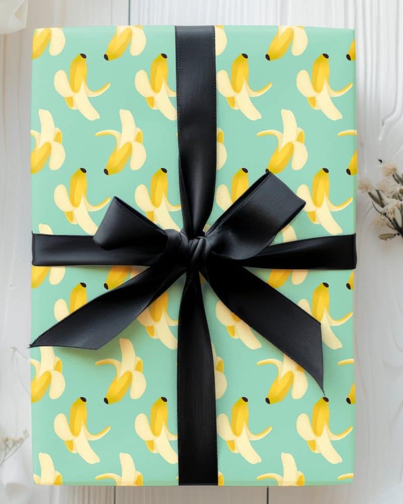 Gift wrapped in light teal paper with a banana pattern and tied with a black ribbon.