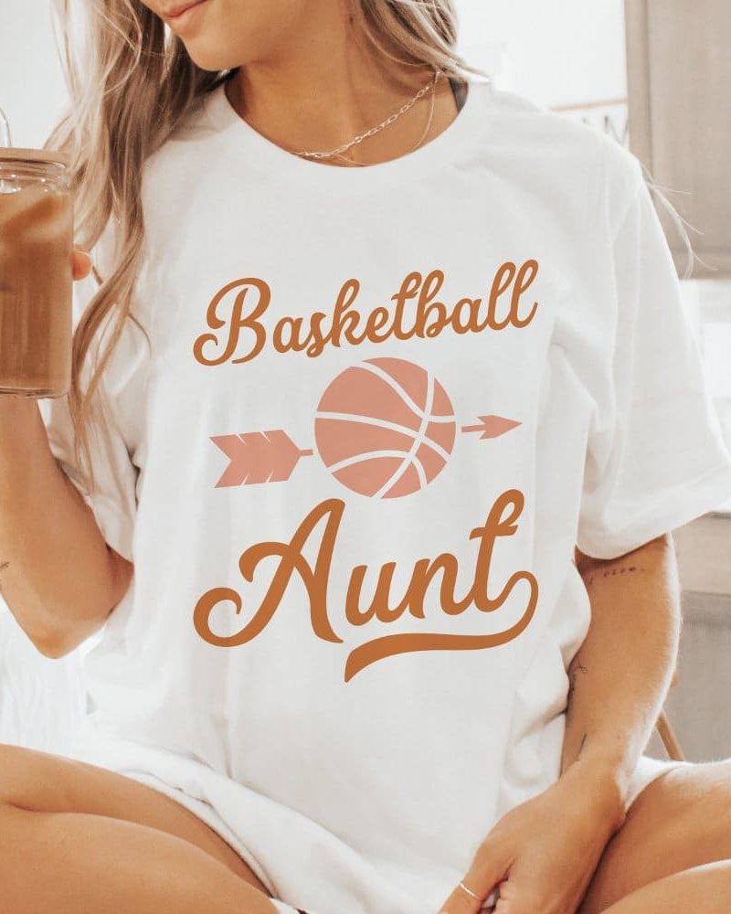 Woman wearing a white t-shirt that says Basketball Aunt with a basketball and arrow design.