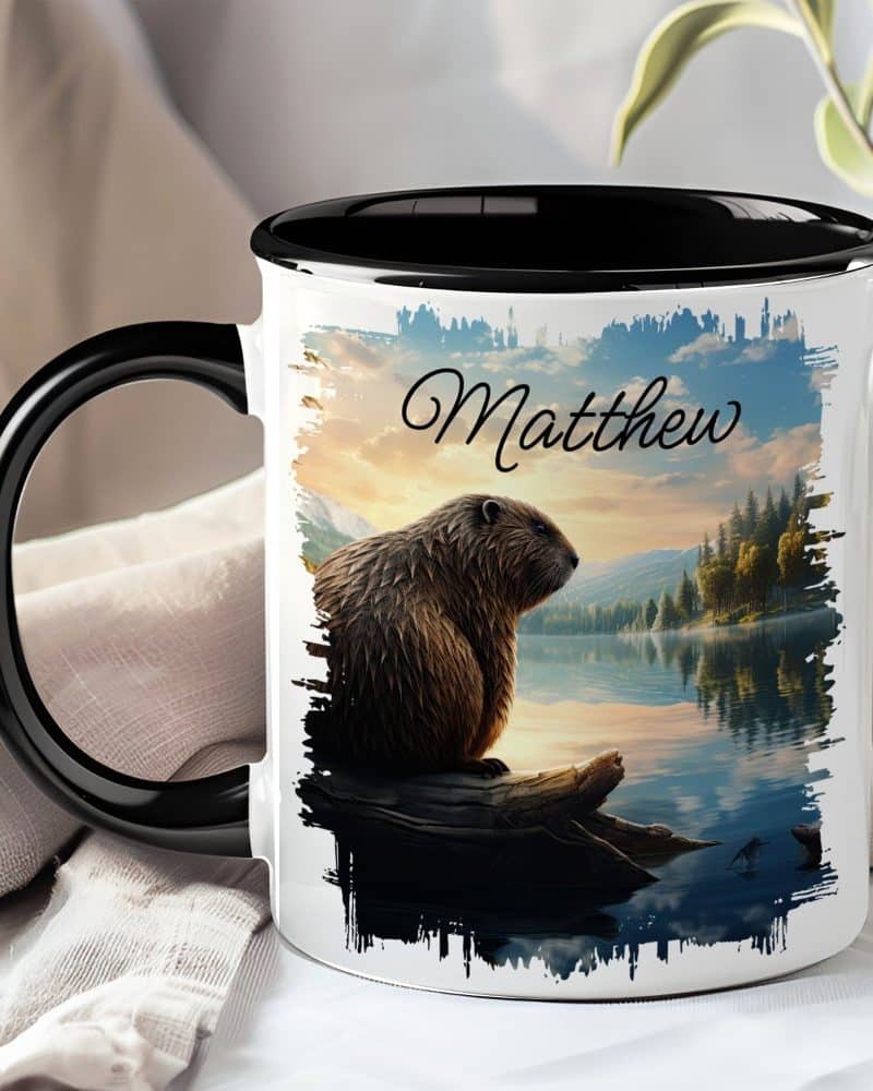 A black-handled mug with a personalized design features a beaver sitting on a log by a lake at sunset, with the name Matthew printed on it.