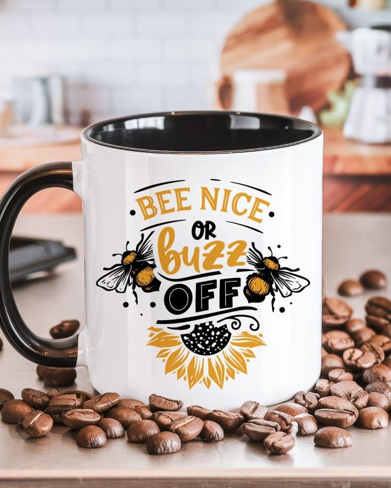 White coffee mug with black handle and interior, featuring a bee-themed design and the text Bee Nice or Buzz Off.