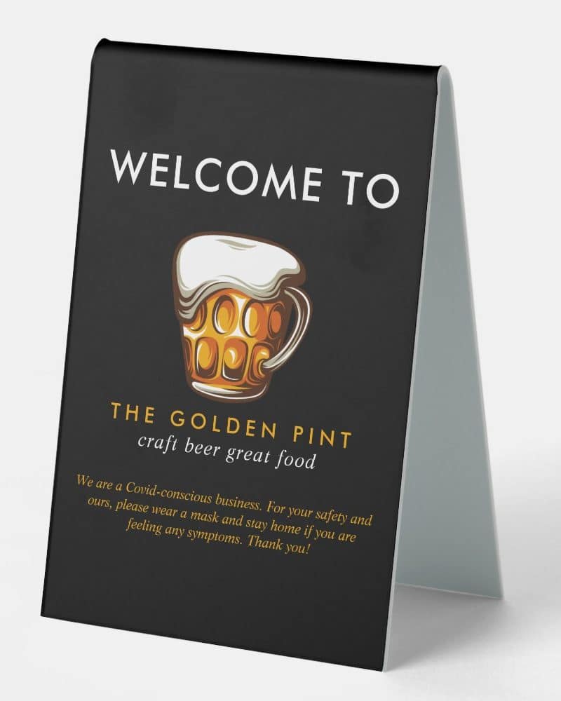 A dark-colored tabletop sign for The Golden Pint, featuring a beer mug graphic and welcoming message.
