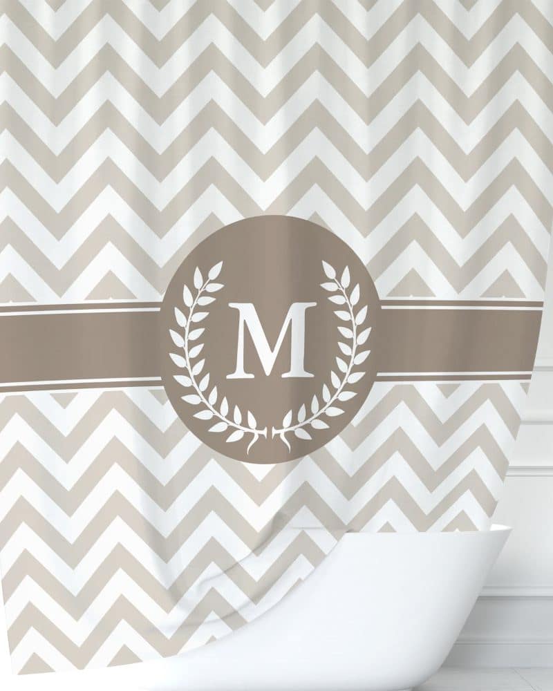 Beige chevron patterned shower curtain with a brown circle monogram featuring the letter M and laurel wreath.