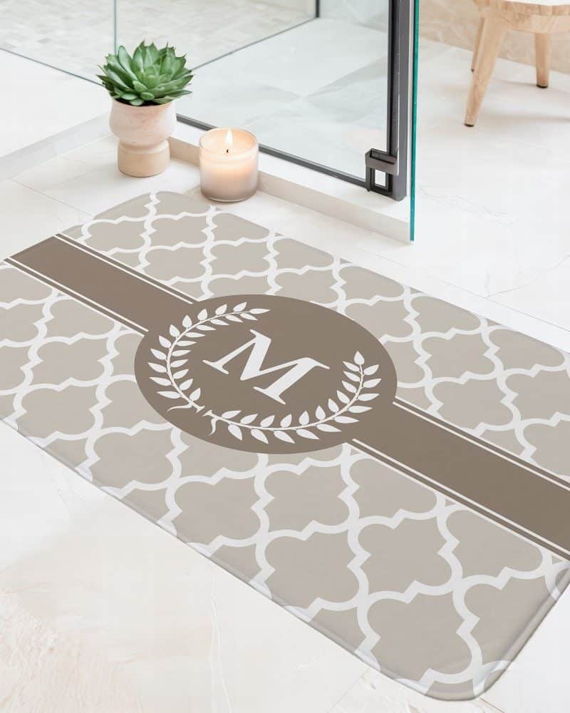 Beige bath mat with a brown stripe and a monogram in a wreath.