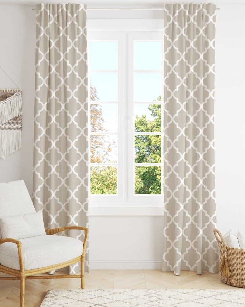Beige curtains with a white quatrefoil pattern hang in front of a window.