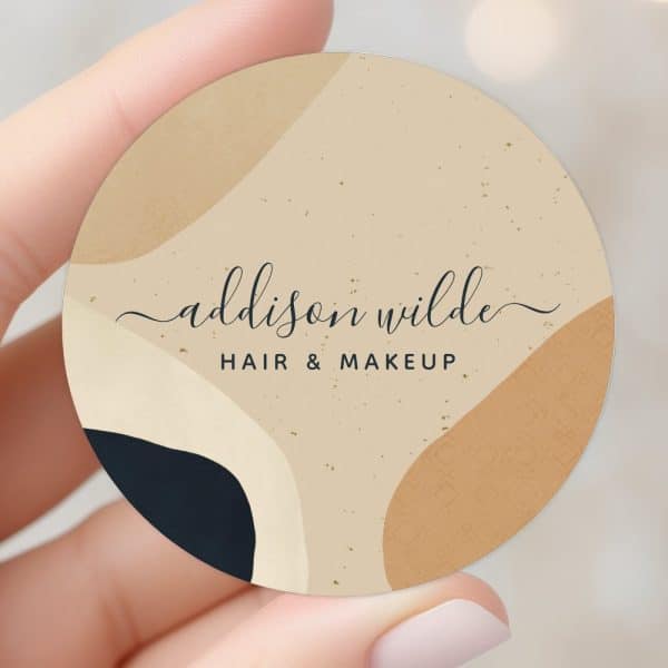 Round Business Card For Addison Wilde Hair &Amp; Makeup, Featuring An Abstract Design In Beige, Brown, And Dark Blue.