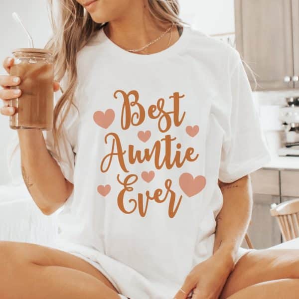 Woman Wearing A White T-Shirt That Says Best Auntie Ever In Orange Lettering With Pink Hearts.