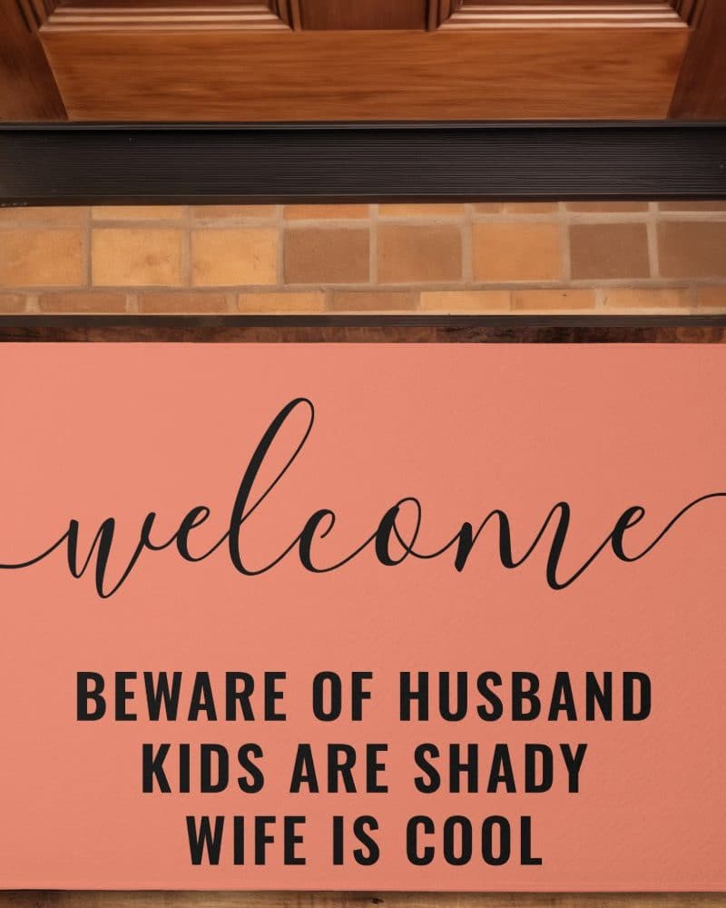 Coral welcome mat with black lettering that says Welcome, Beware of Husband, Kids are Shady, Wife is Cool.