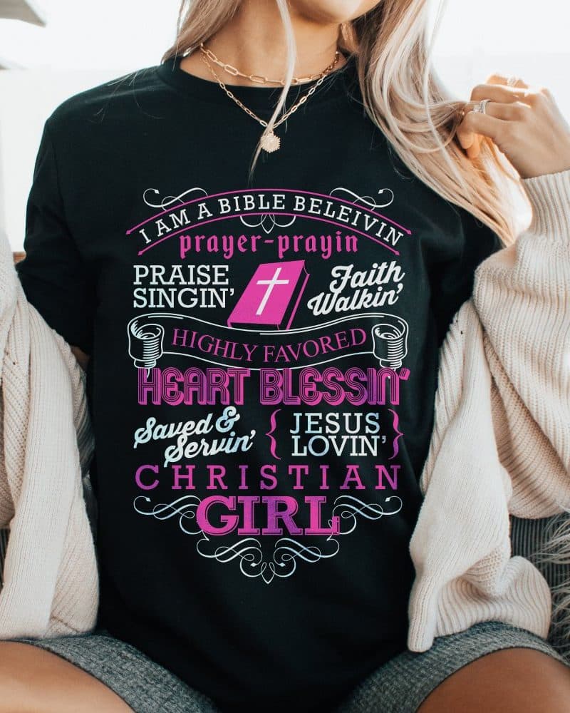 Woman wearing a black t-shirt with pink lettering that says Christian girl and includes other religious phrases.