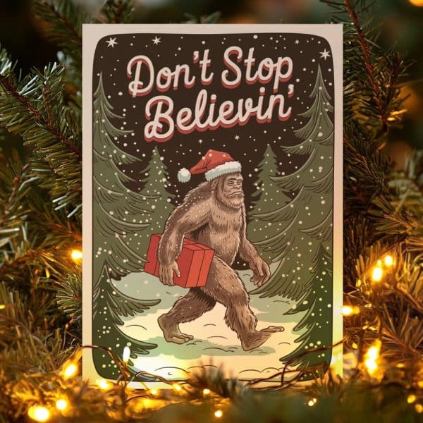 Christmas Card Featuring Bigfoot Wearing A Santa Hat And Carrying A Gift Through A Snowy Forest. The Text Says Don'T Stop Believin'.
