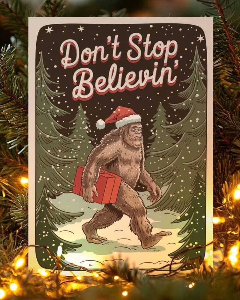 Christmas card featuring Bigfoot wearing a Santa hat and carrying a gift through a snowy forest. The text says Don't Stop Believin'.