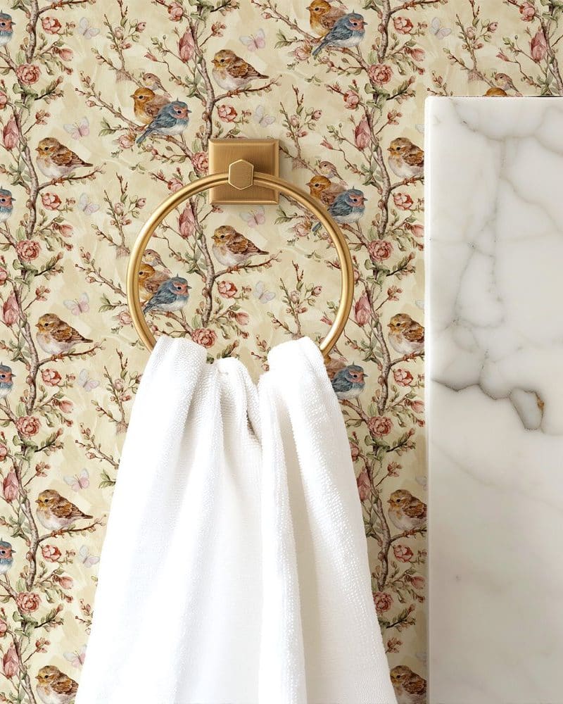 White towel hanging on a gold ring against a floral wallpaper featuring birds and roses.