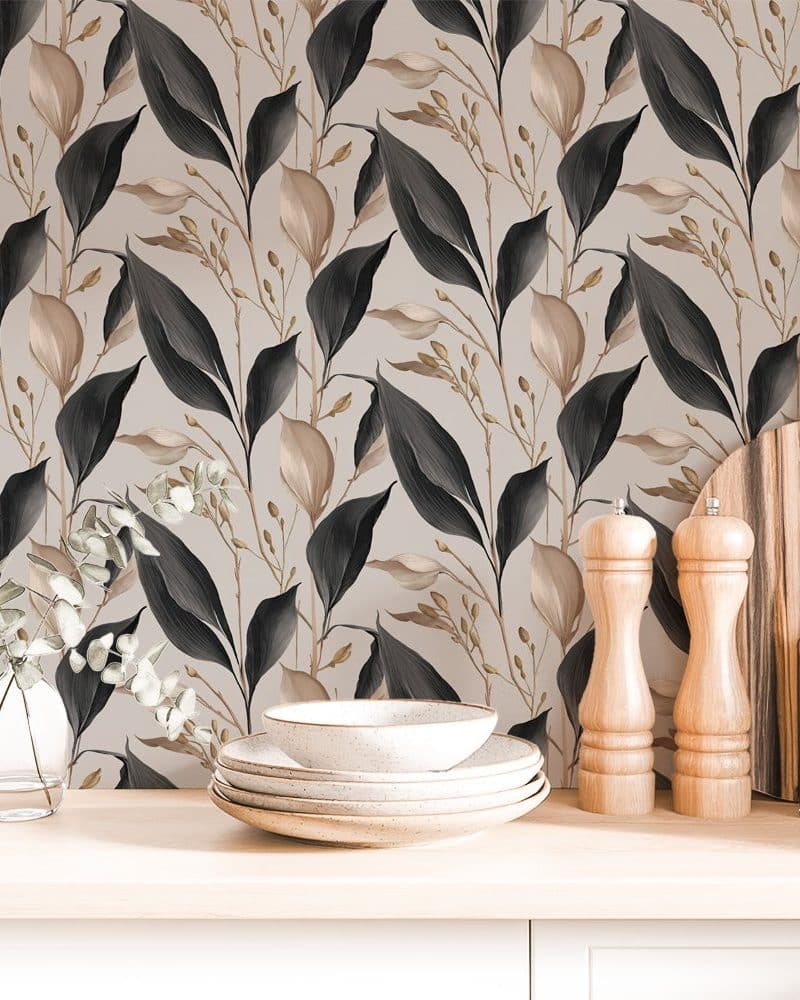 Beige kitchen counter with stacked dishes, salt and pepper shakers, and a cutting board in front of a wall with dark and beige leaf patterned wallpaper.